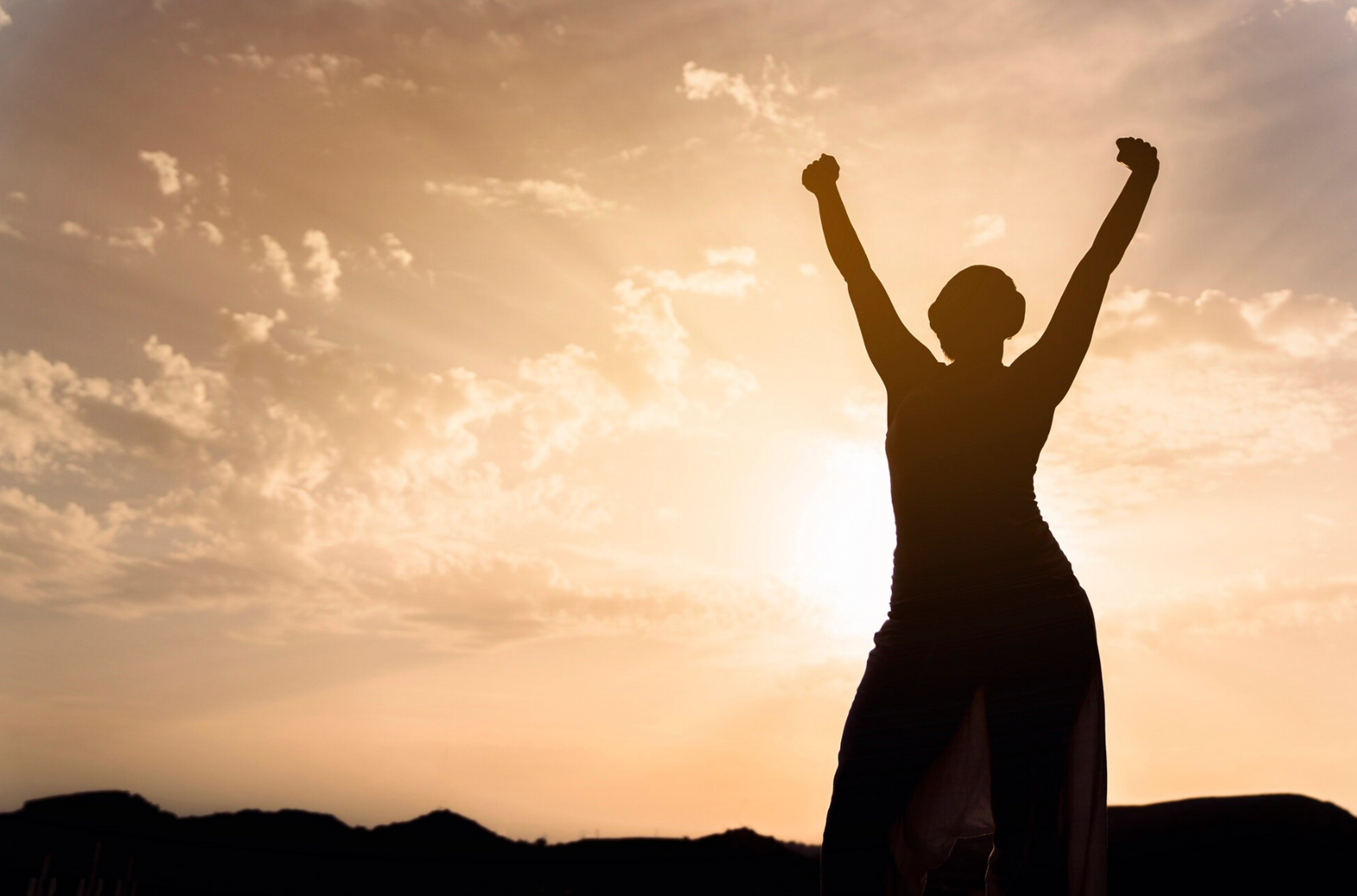 silhouette of a person raising their arms in the air at sunset